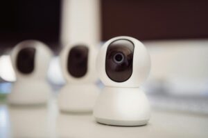 Close-up of three smart home security cameras placed on a white desk indoors.