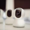 Close-up of three smart home security cameras placed on a white desk indoors.